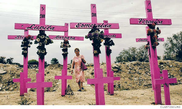 Fotografía de cruces rosas por victimas de feminicidio, al fondo una mujer camina